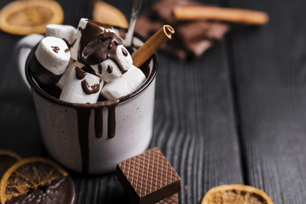 close up of a cup of hot chocolate and marshmallows with a cinnamon stick. 